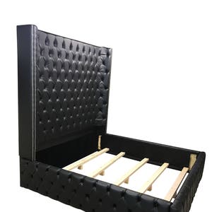 May include: A black upholstered bed frame with a tall headboard featuring a tufted design and silver nailhead trim. The bed frame has a wooden slat support system.