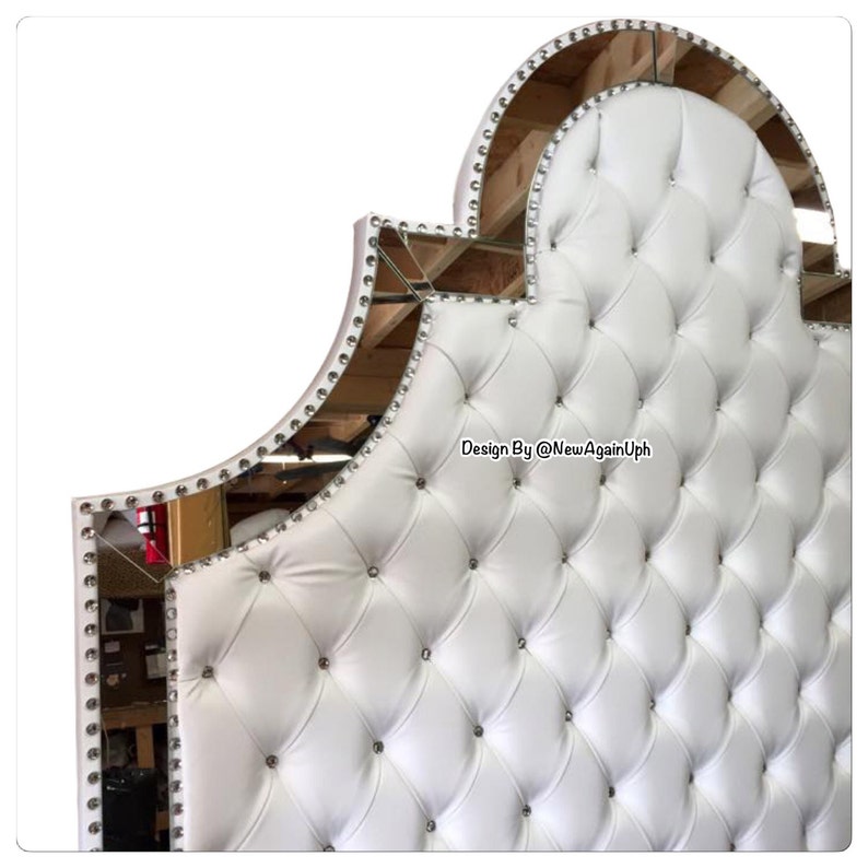 May include: White tufted headboard with a mirrored, arched top. The headboard is decorated with crystal-like studs around the perimeter and on the tufted surface. The text "Design By @NewAgainUph" is visible in the lower right corner.