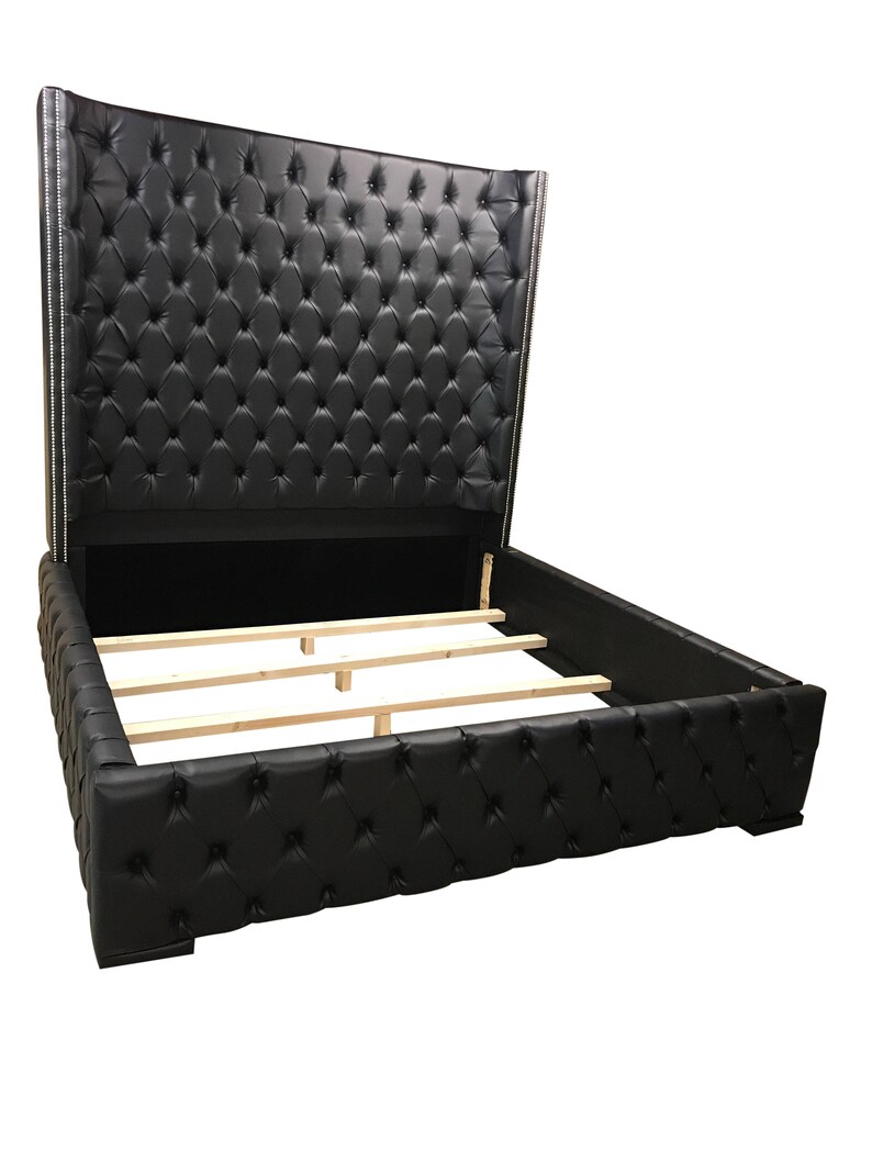 May include: A black leather upholstered bed frame with a tall headboard featuring a tufted design. The headboard is tall and has a curved shape. The bed frame has a wooden slat support system.