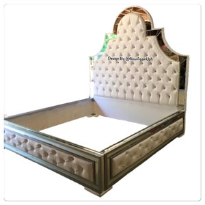 May include: A white tufted headboard with a mirrored frame and a mirrored base. The headboard has a unique arched design and the base has a tufted design. The text "Design By @NewAgainUph" is visible on the headboard.