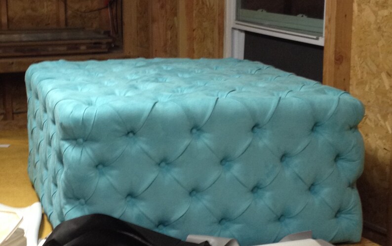 May include: A turquoise tufted ottoman with a square top and a button-tufted design.