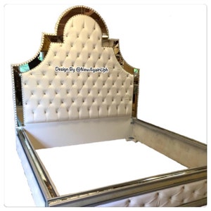 May include: A white tufted headboard with a mirrored frame and a gold trim. The headboard has a diamond-shaped pattern and is accented with silver studs. The text "Design By @NewAgainUph" is visible on the headboard.