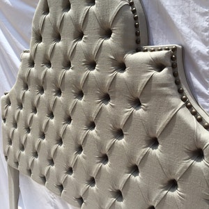 May include: A tufted headboard with a curved top and a linen fabric upholstery. The headboard is decorated with brass nailhead trim.