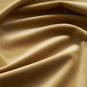 May include: Close-up of a soft, smooth, golden brown fabric with a subtle sheen. The fabric is draped in folds, creating a luxurious and elegant texture.