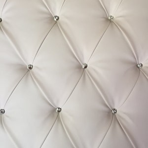 May include: White tufted upholstery with diamond-shaped tufting and clear crystal-like buttons.
