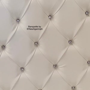 Op de afbeelding: Witte gestoffeerde bekleding met zilveren knoopaccenten. De bekleding heeft een ruitpatroon. De tekst "Banquette by @NewAgainUph" is zichtbaar in het midden van de afbeelding.