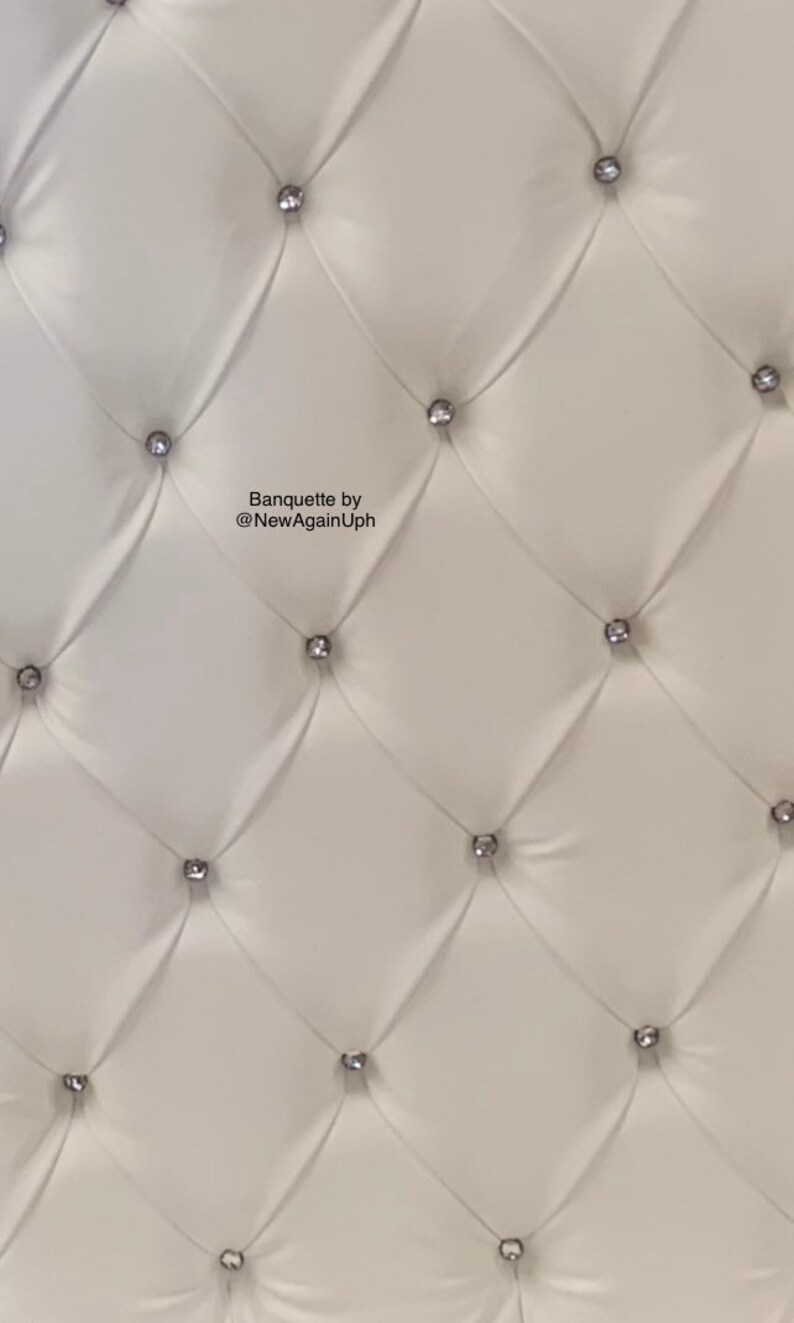 Op de afbeelding: Witte gestoffeerde bekleding met zilveren knoopaccenten. De bekleding heeft een ruitpatroon. De tekst "Banquette by @NewAgainUph" is zichtbaar in het midden van de afbeelding.