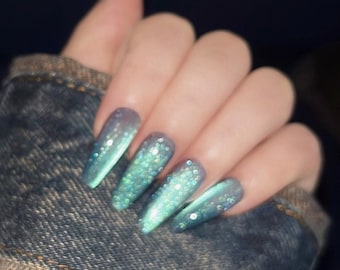 Könnte beinhalten: Nahaufnahme einer Hand mit langen, hellblauen und grünen Ombre-Nägeln mit Glitzer. Die Nägel sind lang und spitz.