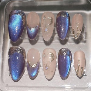 Peut inclure: Un étui en plastique transparent contenant huit faux ongles. Les ongles sont de forme ovale et ont une finition bleu clair irisée. Certains ongles présentent des accents dorés avec un motif de croissant de lune et d'étoile.