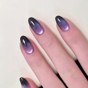 Pode incluir: Unhas de formato oval com um gradiente suave que transita de uma base preta profunda na cutícula para um tom roxo vibrante nas pontas. O acabamento é brilhante e reflexivo, criando um efeito de olho de gato que capta a luz.
