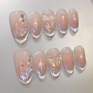 Puede incluir: Conjunto de diez uñas postizas ovaladas con un diseño degradado. Las uñas están decoradas con purpurina, pedrería y abalorios de mariposa.
