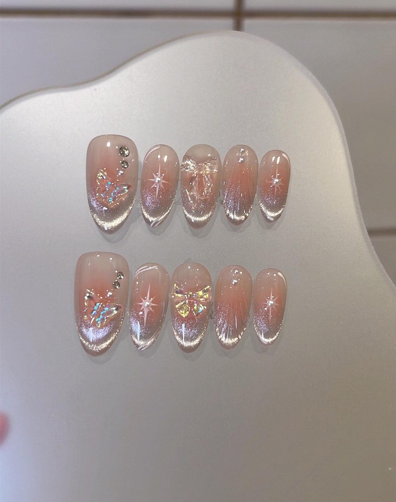 May include: Set of ten false nails with a clear base and a variety of designs, including butterflies, stars, and glitter.