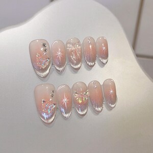 May include: Set of ten false nails with a gradient pink and white design. Each nail features a different design, including butterflies, stars, and rhinestones.