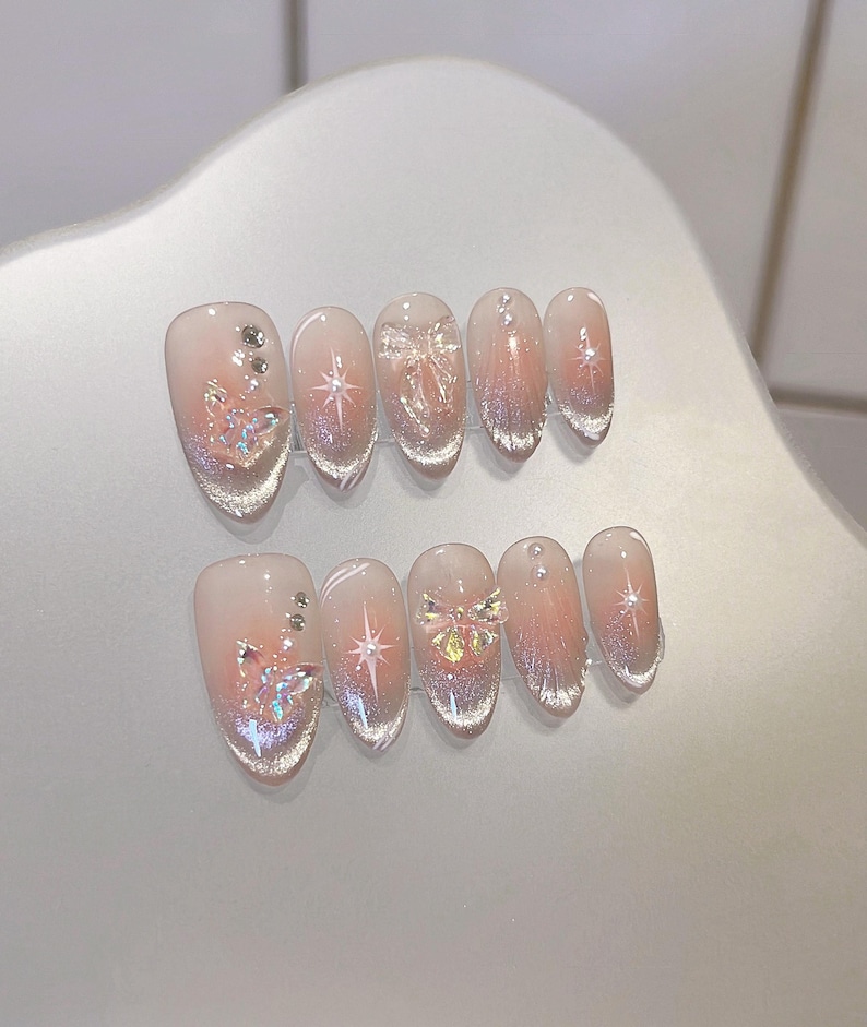 May include: Set of ten false nails with a gradient pink and white design. Each nail features a different design, including butterflies, stars, and rhinestones.