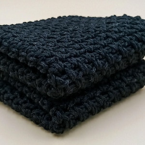 May include: Two black crocheted dishcloths stacked on top of each other. The dishcloths are made with a textured stitch.
