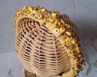 Puede incluir: Una diadema amarilla con un diseño de cuentas. La diadema está decorada con cuentas amarillas y doradas, lentejuelas y pequeñas flores.