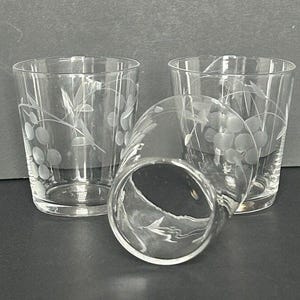 May include: Three clear glass shot glasses with an etched floral design. The glasses are stacked on top of each other.