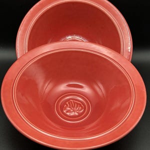 Könnte beinhalten: Zwei rote Keramikschalen mit einem Blattdesign auf dem Boden. Die Schalen sind ineinander verschachtelt.