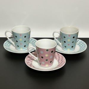 以下が含まれることがあります： 水玉模様の陶磁器製カップとソーサーの3客セット。2客は水色地にダークブラウン、ピンク、黄色の水玉模様で、同柄のソーサー付き。もう1客はピンク地にダークブラウン、水色、黄色の水玉模様で、ピンクのソーサーがセットになっています。