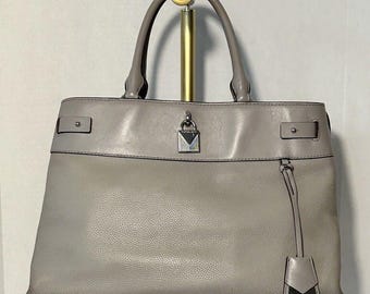 May include: A gray leather tote bag with a silver lock and key detail. The bag has a top handle and a detachable shoulder strap.