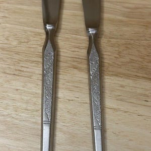 May include: Two silver butter knives with an ornate floral design on the handles.