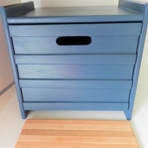 May include: A blue wooden storage box with a handle and four drawers. The box is sitting on a wooden cutting board.