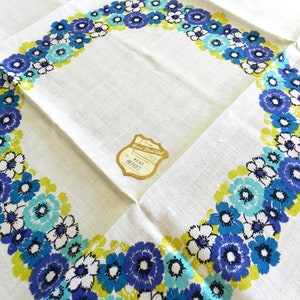 May include: White tablecloth with a blue, green, and white floral border. The tablecloth has a Home Beautiful label attached to it. The label reads "Home Beautiful All Linen Cotton Tablecloth 4740 61/2 x 61/2"