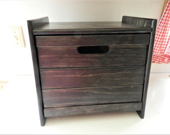 May include: A dark brown wooden storage box with a hinged lid and a cutout handle. The box has a rustic, farmhouse style.