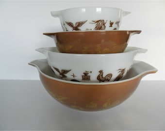 May include: A set of four stacked mixing bowls with handles. Two bowls are white with brown printed graphics of eagles, roosters, coffee grinders, and wheat. Two bowls are solid brown with gold-toned graphics of the same motifs.