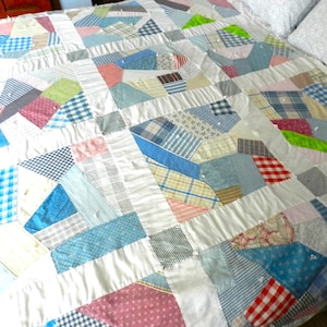 May include: A patchwork quilt made from various fabrics in shades of blue, white, and pink. The quilt is made up of squares and rectangles of different sizes and patterns, creating a unique and interesting design.
