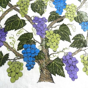May include: A white fabric with a printed design of a grape vine. The vine has a brown trunk and branches, with clusters of green, blue, and purple grapes. The leaves are green, and the design is signed "Lou Long".