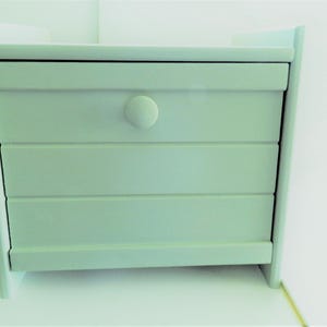 May include: A white bread box with a single drawer and a white knob. The bread box has a slightly distressed look and is made of wood.