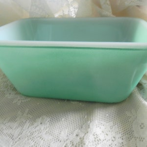 May include: A vintage green Pyrex baking dish with a white rim. The dish is made of glass and has a rectangular shape.