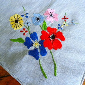 May include: A blue linen handkerchief with embroidered flowers in red, yellow, blue, and pink.
