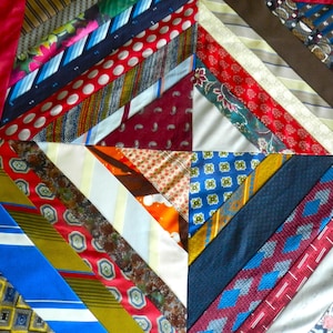 May include: A patchwork quilt composed of various patterned neckties in shades of red, blue, yellow, and brown. The diagonal arrangement of the ties creates a geometric design, with a red border.