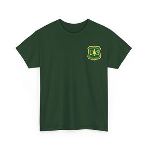 May include: Dark green t-shirt with a Forest Service emblem on the left chest. The emblem is a shield shape with a green tree and the letters "UAS" in the centre, surrounded by yellow text.