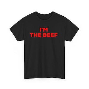 May include: Black t-shirt featuring the red text "I'M THE BEEF". The text is in a bold, sans-serif font. The t-shirt has a crew neck and short sleeves, made of a soft fabric. A casual, everyday garment.