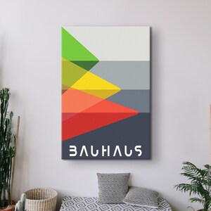 May include: A geometric abstract art print with a Bauhaus design. The print features a series of overlapping triangles in shades of green, yellow, orange, red, and gray. The word "Bauhaus" is printed in white at the bottom of the print.