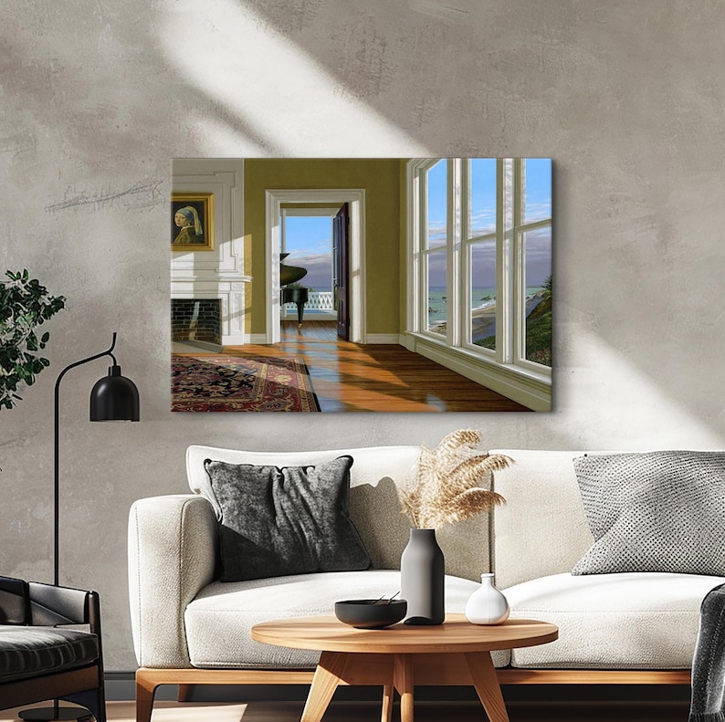 Op de afbeelding: Een ingelijste canvas print met een interieursc&egrave;ne met uitzicht op zee. De kamer heeft een open haard, een tapijt en een deuropening naar een balkon. Grote ramen bieden uitzicht op de zee en de lucht. De kamer is ingericht in neutrale tinten.