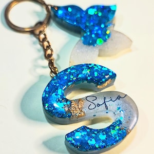 May include: A blue and white glitter resin keychain with a butterfly charm and the name "Sofia" written on it.