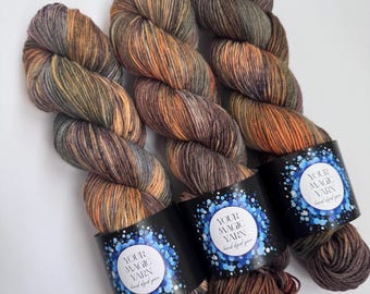 May include: Three skeins of hand-dyed yarn in a mix of earthy tones: brown, orange, and green. Each skein is wrapped with a black label that reads "YOUR MAGIC YARN hand dyed yarn" in white and blue.