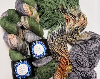 May include: A selection of hand-dyed yarn in shades of green, grey, and orange. Two skeins are labelled "YOUR MAGIC YARN hand dyed yarn" with a blue and white design. The yarn is arranged in skeins and loose strands, displaying the colour variations.