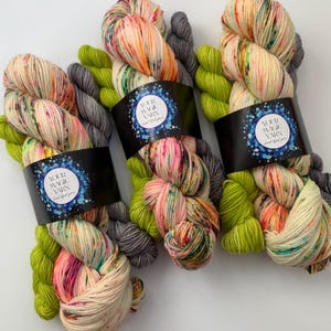 May include: Three skeins of hand-dyed yarn in a variety of colours, including green, grey, and a multi-coloured skein with pink, orange, and yellow. The yarn is labelled "Your Magic Yarn".