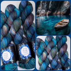 Op de afbeelding: Handgeverfd garen in tinten blauw, blauwgroen en paars. Het garen is gerangschikt in strengen en heeft een gevarieerd kleurenpatroon. De afbeelding bevat ook een kleine boot op een water en de tekst "YOUR MAGIC YARN hand dyed yarn".