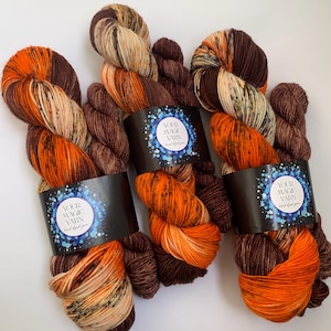 May include: Three skeins of hand-dyed yarn in orange, brown, and cream colors. The yarn is wrapped around labels that say "Your Magic Yarn".