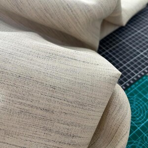 May include: Close-up of a beige fabric with a subtle woven texture. The fabric has a slightly rough, natural feel.