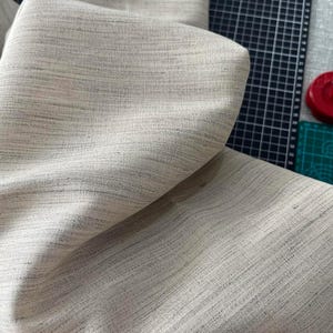 May include: Close-up of a beige fabric with a subtle woven texture. The fabric is folded and draped over a surface.