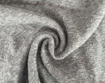 May include: Close-up of a gray textured fabric with a subtle white fleck. The fabric is folded and draped, showing its soft and drapey texture.