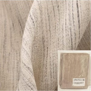 May include: Close-up of a beige woven fabric with a textured appearance. The fabric has a subtle pattern of vertical lines and a natural, neutral color. A packaged sample of the fabric is visible in the lower right corner, with the brand name "HAUTICO" on the label.