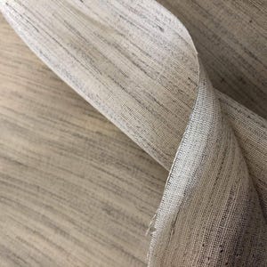 May include: Close-up of a beige fabric with a subtle woven texture. The fabric is folded over itself, creating a soft, flowing drape.